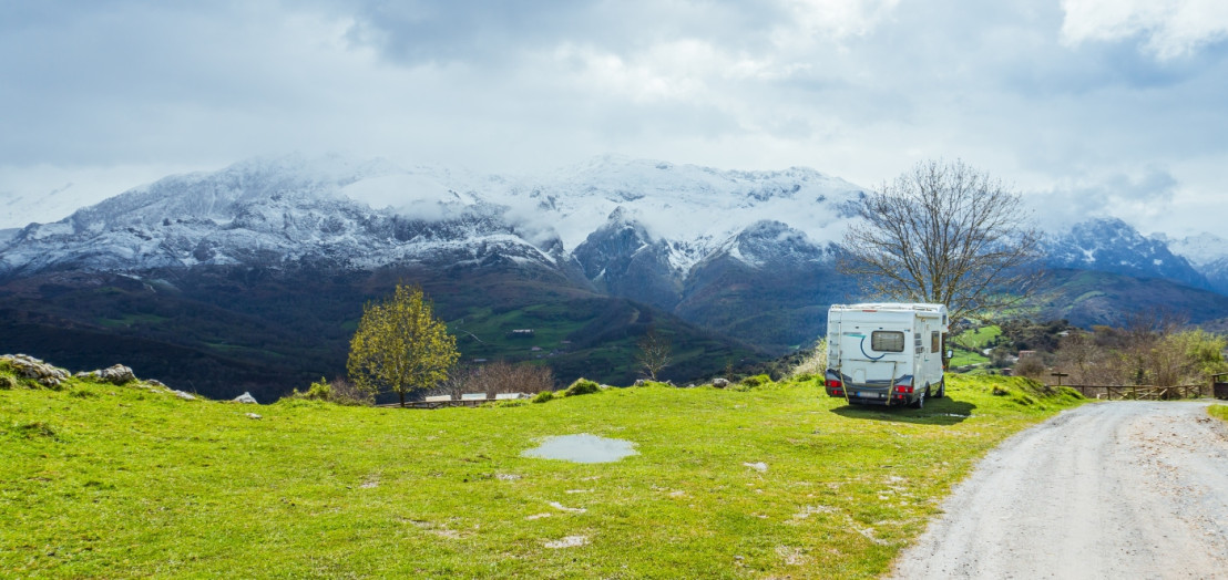 Camper op een grasveld geparkeerd met een heel mooi uitzicht op de bergtoppen bedekt met sneeuw.